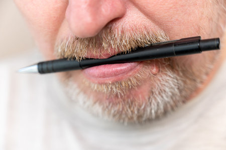 The bottom of a man's face with a pencil in his mouth. Man holding plastic black pencil or pen with...