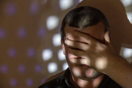 A man covered his face with his hand. Portrait of a middle-aged man against a wall. A light and...