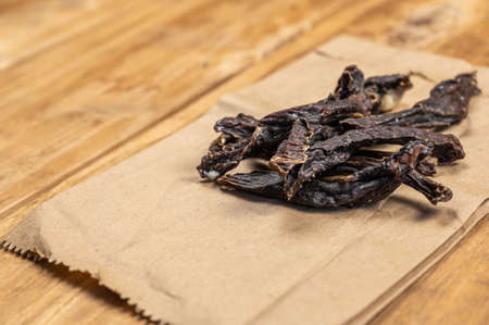 Sticks of dried meat against a wooden background. Pieces of dried beef or jerky. brown paper bag. Ready-to-eat food. selective focus.の写真素材