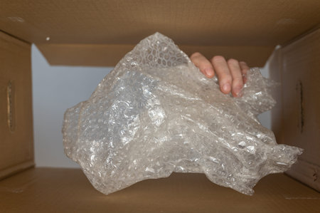 A man's hand puts wrap in a cardboard moving box. Plastic wrap or filler for postage. bottom view....