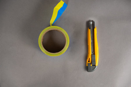 Yellow paper cutter and adhesive tape. The hand tool lies on a gray uneven surface. Blue and yellow...