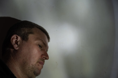 Portrait of a depressed middle-aged man with his head down. Unshaven man leaning against the wall....