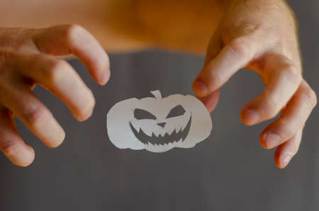 White Paper Halloween Pumpkin and hands with fingers bent in terror. Halloween paraphernalia cut with scissors from sheet of paper. Flying in ir Silhouette Smiling intimidating face. man's handsの写真素材