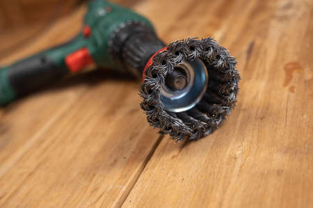 Knot cup wire brush installed in the cam of the power drill chuck. Tool for woodworking, sanding, removing rust from various surfaces. inside the room. close-up. selective focus.の写真素材