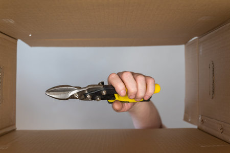 A man's hand puts a sheet metal cutter in a cardboard moving box. Hand tool with yellow handles....