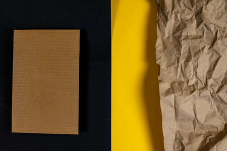 Rectangular piece of brown cardboard on black. Crumpled wrapping paper on the right side of the photo against yellow. Copy space for text and design elements. top view.の写真素材