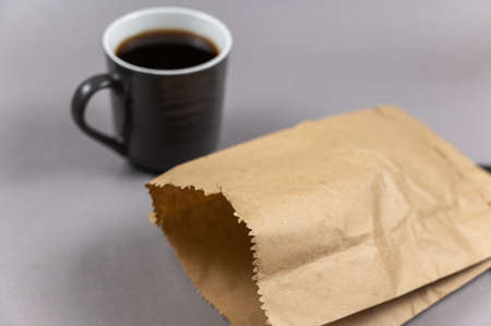 A brown paper bag and a cup of coffee on grey. A full cup of hot, invigorating drink. A lunch bag of food. selective focus.の写真素材