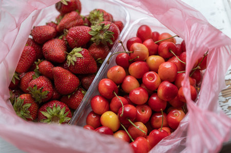Ripe strawberries and sweet cherries inside a pink plastic bag. New crop of red berries in clear...