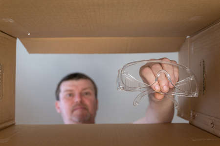 Man pulls safety glasses out of cardboard box for moving. Personal protective equipment. bottom view. inside view. close-up. selective focus.の写真素材