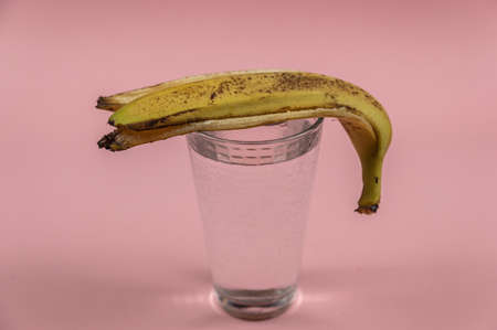 A glass of water and a banana peel on a pink background. A full glass of drinking water. close-up. selective focus.の写真素材
