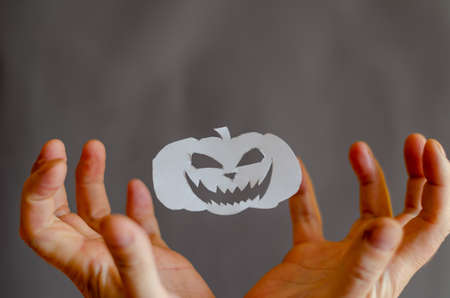 White Paper Halloween Pumpkin and hands with fingers bent in terror. Halloween paraphernalia cut with scissors from sheet of paper. Flying in ir Silhouette Smiling intimidating face. man's handsの写真素材