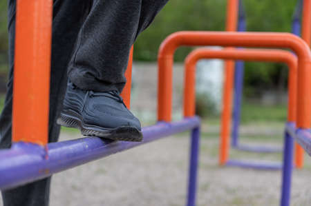 The lower section of a mature man engaged in restorative gymnastics on the sports ground. The man's legs are standing on the blue and orange bars. Recovery from a leg injury. rehabilitation. outsideの写真素材
