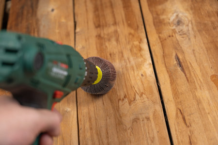 Man processes wooden boards with power tool. Flap wheel in the cam of the electric drill chuck. Tool...