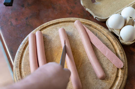 A man is cutting a sausage with a knife. An adult male cuts along a sausage on a cutting board. Cooking a meal. Selection trick.の写真素材