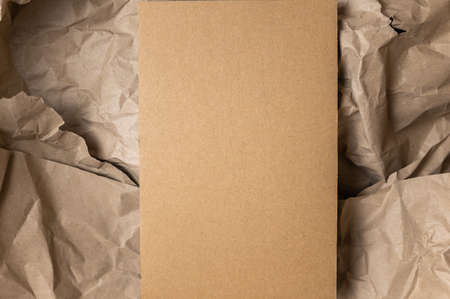 Rectangular piece of brown cardstock against crumpled wrapping paper. Copy space for text and design elements. Minimalist composition for various design tasks. top view.の写真素材