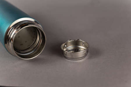 Modern thermos and silver teapot against a gray background. Cylindrical vacuole flask in turquoise color. Container for hot and cold drinks. Equipment for sports, hiking, travel.の写真素材