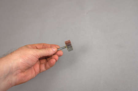 A man's hand holds the Sanding Blade Wheel. A tool for woodworking as well as stripping surfaces of corrosion, scale or rust. side view. gray background. selective focus.の写真素材