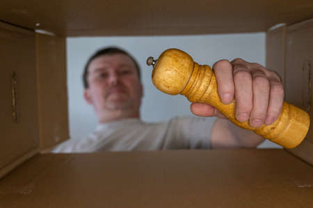 A man pulls a wooden spice mill out of a cardboard moving box. Yellow handmill for peppers, layers and other spices and condiments. bottom view. inside view. close-up. selective focus.の写真素材