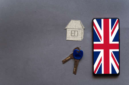 Smartphone, keys to the door and a small paper house in grey. The flag of the United Kingdom on the screen of the device. Change of residence, purchase of real estate d to the UK conceptの写真素材