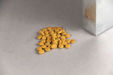 A silver rectangular box against a gray background. Pet food spilling out of the hole. Dry pellet food. pet food. selective focus.の写真素材