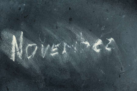 Semi-erased word NOVEMBER on black chalkboard. handwritten word. Fuzzy letters on a black surface. The concept of alternating months of the year. Calendarの写真素材