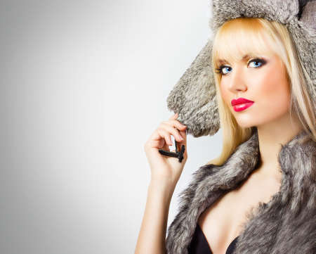 Beautiful blonde girl in fur hat on grey backgroundの写真素材