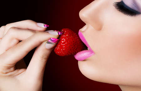 Beautiful girl with pink nails eating strawberryの写真素材