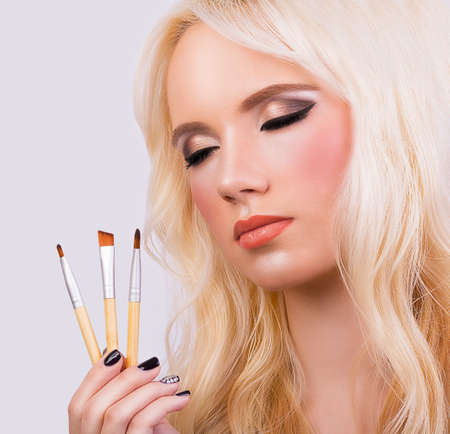 Beautiful blonde girl with makeup brushes on grey backgroundの写真素材