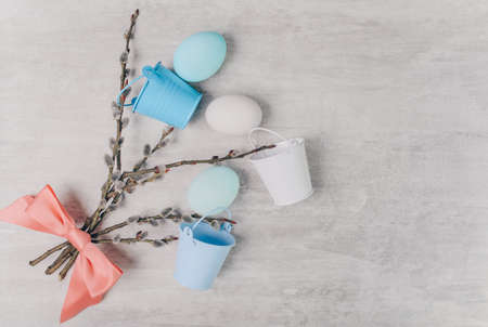 Easter blue eggs and willow branches tied with a pink ribbon and with small buckets on a grey wooden table.の写真素材