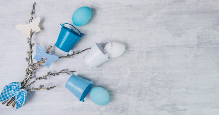 Easter blue eggs and willow branches tied with a blue ribbon and with small buckets on a grey wooden...
