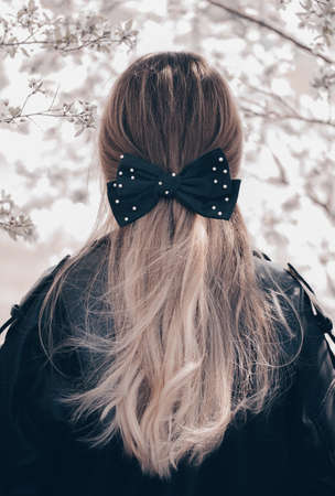 Portrait of a beautiful young woman with long wavy hair with black bow. back view.の写真素材