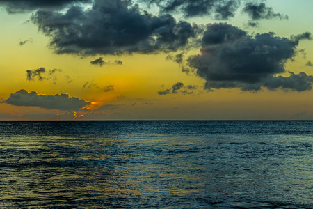 Bright sun at sunset or dawn over the water of the Pacific Ocean. The sun's rays during the golden hour in the morning or evening lit the fluffy cumulus clouds in a sky. The calm atmosphere of heavenの写真素材