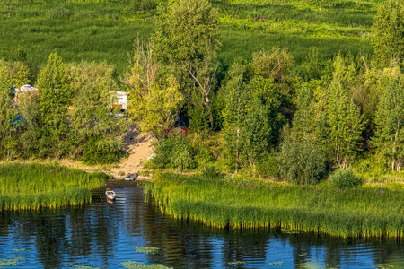 Quiet backwater overgrown with reeds, small fishing boat on the Volga River near the city of Samara, Russia. Blue water, sandy shore, tree, forest, bush. Quiet summer morning with light sky.の写真素材