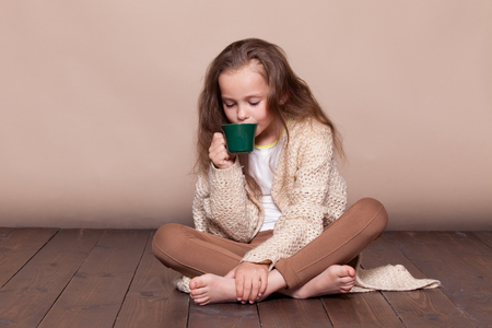 a little girl sitting on the floor and drinking teaの写真素材