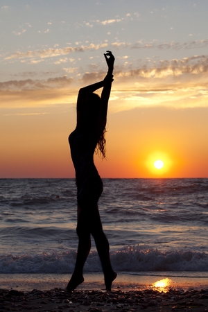 Silhouette girls by the sea at sunsetの写真素材