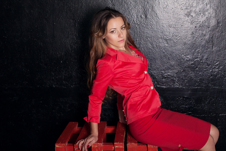 beautiful girl in a red dress at a black wallの写真素材