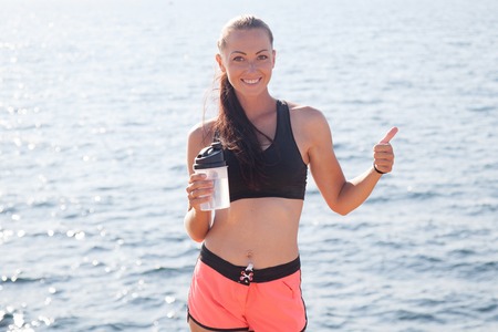 girl drinks water after sports and shows a thumbs upの写真素材