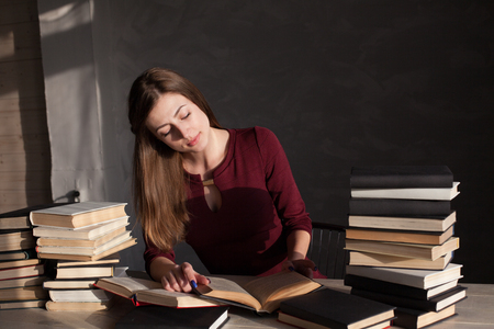 the girl sitting at the table reading a lot of booksの写真素材
