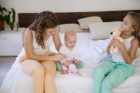 Sisters play with the baby on the bed in the bedroomの写真素材