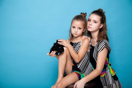 two fashionable girls posing with a camera on a blue background