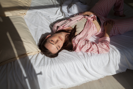 brunette woman in pink Pajamas lying on bedの写真素材
