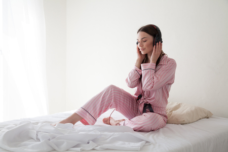 brunette woman in pajamas listening to music lies in bedの写真素材