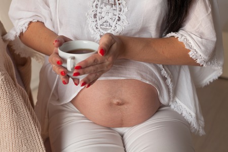 the stomach of a pregnant woman hands holding a cup of tea or coffeeの写真素材