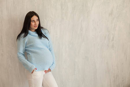 Portrait of beautiful pregnant woman in the blue jacket on a grey backgroundの写真素材