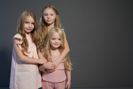 three beautiful little girls sisters portrait fashion grey backgroundの写真素材