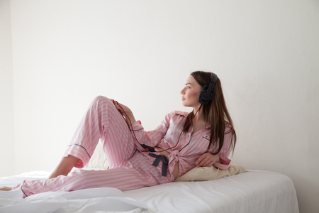 woman in pajamas on the bed listening to music headphonesの写真素材