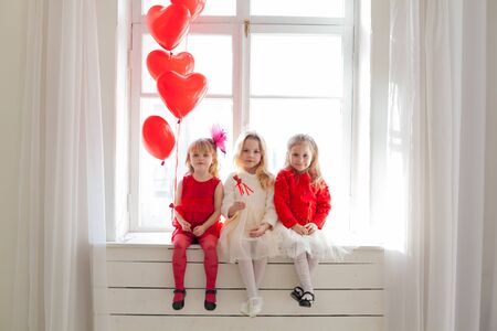 Three little girls sitting with red heart balloonsの写真素材