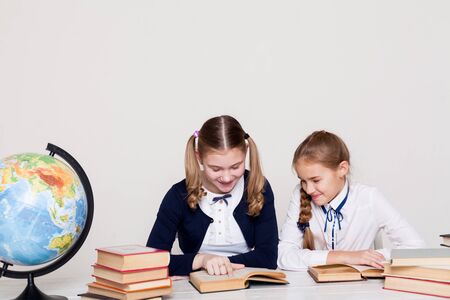two schoolgirl girls with books at the school deskの写真素材