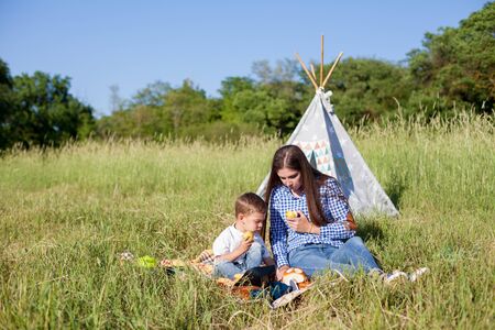beautiful woman with her son on a picnic in a field near the forestの写真素材