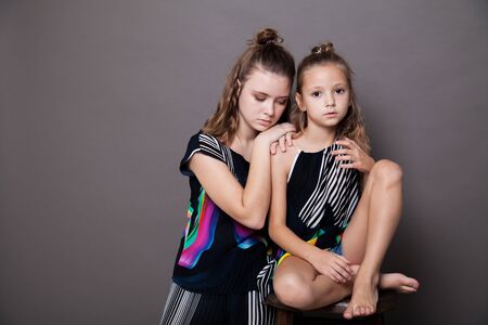Portrait of two beautiful fashionable sisters girls on a gray backgroundの写真素材